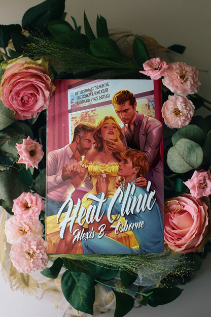 An aesthetic photo of the heat clinic special edition hardcover showing the illustrated side of the dust jacket with Emily, arcus, Tom, and Sam at the clinic. The book is surrounded by pink flowers and geenery.