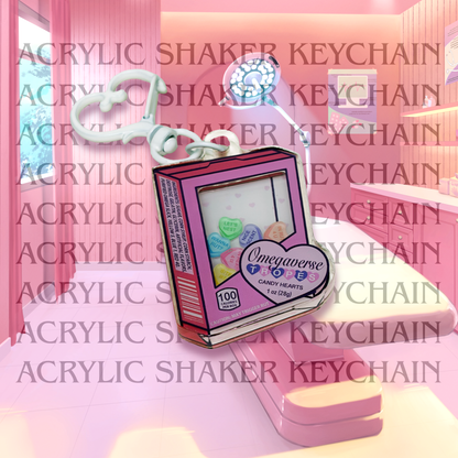 Acrylic shaker keychain shaped like a candy heart box that says omegaverse tropes. The candy hearts inside say let's nest, in rut 4 u, in heat 4 u, nice scent, bite me, and wanna rut?