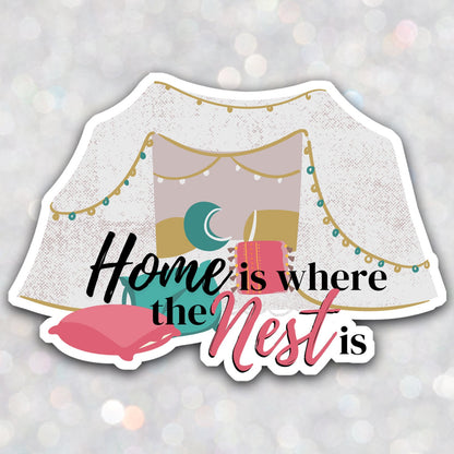 A vinyl omegaverse themed sticker that says "home is where the nest is" with a pillow fort full of teal, pink, and yellow pillows and string lights.